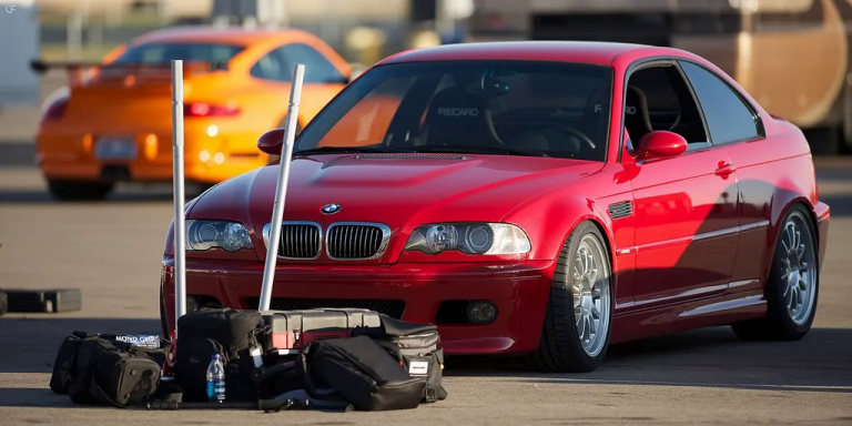 Red BMW parked in a parking lot with a bunch of car equipment in the front